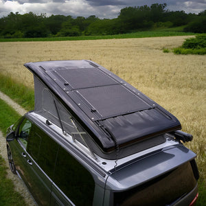 VW T7 Beach Camper with pop-up roof and solar panel in a scenic field